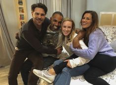 a group of people sitting on top of a bed posing for the camera with their arms around each other