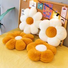 three stuffed flowers sitting on top of a bed next to a bulletin board with pictures