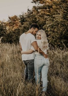 a man and woman are standing in the tall grass with their arms around each other