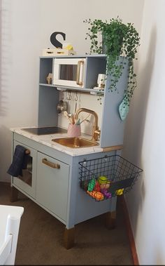 a toy kitchen with a sink, cupboards and potted plant in the corner