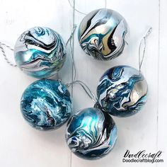 marbled glass ornaments are hanging on a white wooden surface with silver and blue swirls