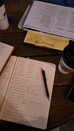 an open notebook and pen on a table next to a coffee cup with a cell phone