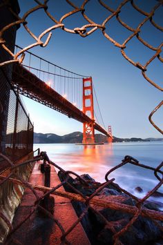 the golden gate bridge is seen through a chain link fence