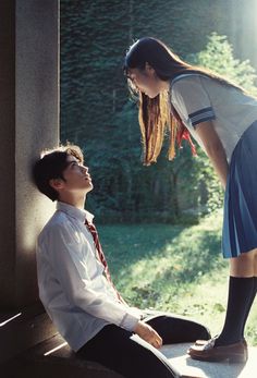 a young man sitting on the ground next to a woman in a dress and tie