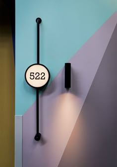 a black clock mounted to the side of a blue and purple wall next to a light