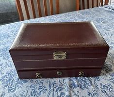 an old brown leather suitcase sitting on top of a blue and white tablecloth covered table