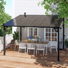 a patio with a table and chairs under a black awning next to a white house