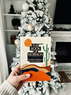 a person holding up a book in front of a christmas tree with the title, the book of mormon