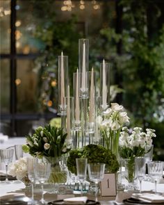 an arrangement of flowers and candles on a table with place settings in front of them