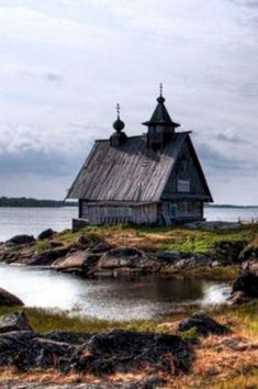 an old wooden building sitting on top of a lush green field next to the ocean