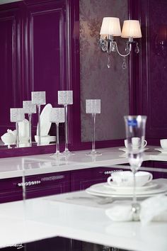 a kitchen with purple cabinets and white counter tops in front of a large mirror on the wall