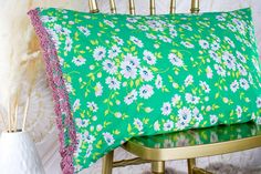 a green pillow with pink and white flowers sitting on a chair next to a vase