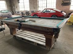 an old pool table is being worked on in a garage with other cars parked behind it