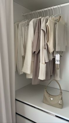 the closet is full of sweaters, pants and handbags on hangers next to a purse