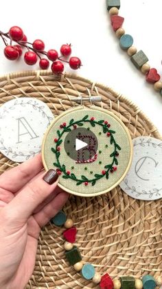 a person is holding up a small embroidery project on a wicker mat with other items around it