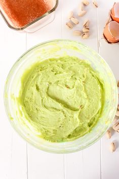 a bowl filled with green guacamole next to an egg shell and other ingredients