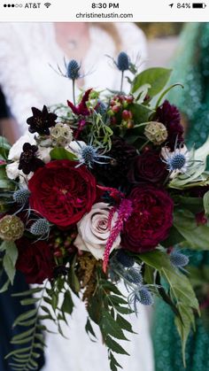 a bride holding a bouquet of red and white flowers with greenery in her hands