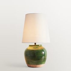 a green and yellow vase with a white shade on it's side, sitting next to a lamp