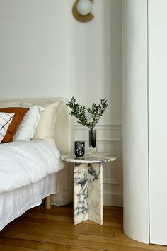 a white bed sitting next to a table with a vase on it's side