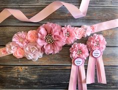 some pink flowers and ribbons on a wooden table with a name tag attached to it