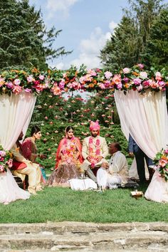 a group of people sitting on top of a lush green field under a canopy covered in flowers