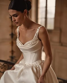 a woman in a white wedding dress sitting on a bench looking down at her hand