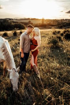 a man and woman standing next to each other in a field with a white horse