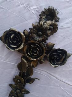 several metal flowers are arranged on a white tablecloth with gold foil leaves and pine cones