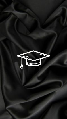 a graduation cap on top of a black satin fabric with a white outline in the center