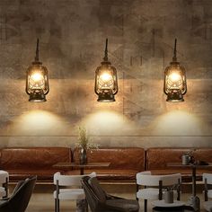 three lamps hanging from the side of a wall next to couches and tables in a restaurant