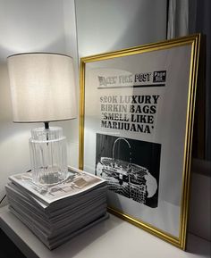 a stack of magazines sitting on top of a table next to a framed poster and lamp