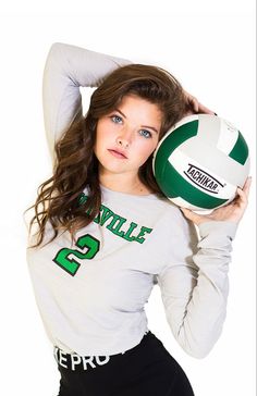 a woman holding a volleyball ball in her right hand and posing for the camera with one arm behind her head