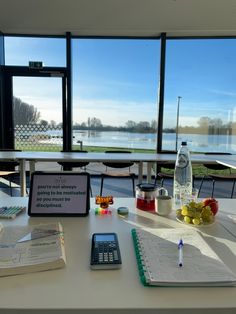 there is a cell phone on the table next to some books and other items in front of a large window