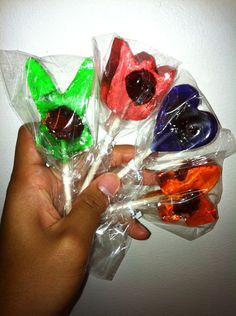 a hand is holding four lollipops in plastic wrappers with colorful candies on them