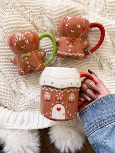 someone is holding two mugs with gingerbread houses on them