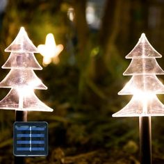 two lighted christmas trees in the woods with lights on each one and a small solar panel attached to them