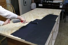 a woman is painting the top of a wooden table with black paint on it, while another woman stands in the background