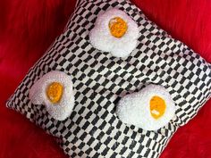 two fried eggs on a black and white checkerboard pillow with orange felt eyes