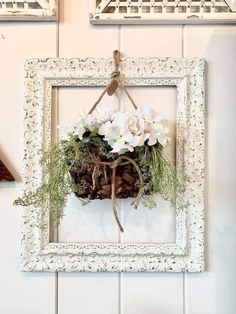 a white frame hanging on the wall with flowers in it