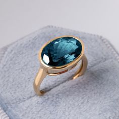 "5 Carat London Blue Topaz Ring, Something Blue For Her, December Birthstone, Bezel Set East West Engagement Ring, Chunky Gold Statement Ring This ring features a 5 ct oval London Blue topaz set in 14k or 18k Solid gold. The design is a bezel-style setting but with an east-west setting. The Horizontally set Oval gives the design a modern edge while maintaining the classy look of a bezel ring. The stone is a high-quality stone with a good cut and a mesmerizing color. The London blue topaz, that we use,  is 100% natural stone with no treatment. London Blue Topaz is a December birthstone, a perfect present for your loved ones.  The ring can be customized in yellow gold or white gold. Please select from the drop-down menu. ★ ★  CUSTOM/DUTY-FREE SHIPPING WORLDWIDE, BUYERS DON'T HAVE TO PAY ANY Luxury Fine Jewelry Birthstone Ring With Smooth Bezel, Luxury Oval Topaz Ring With Stone Setting, Luxury Birthstone Ring With Smooth Bezel For Gift, Blue Topaz Ring With Bezel Setting As Gift, Blue Topaz Ring With Bezel Setting For Gift, Oval Turquoise Sapphire Ring As A Gift, Sapphire Blue Topaz Rings With Bezel Setting, Blue Oval Topaz Ring With Bezel Setting, Gift Turquoise Sapphire Ring With Accent Stones