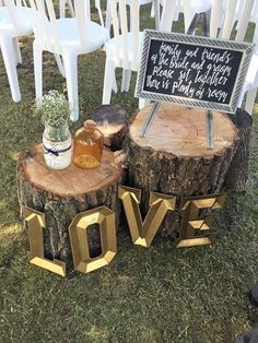 two wooden stumps with love signs on them sitting in the grass next to white chairs