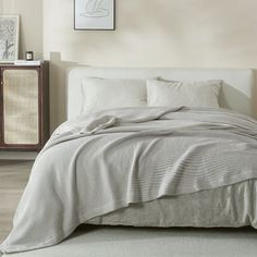 a bed with white sheets and pillows on top of it next to a dresser in a bedroom