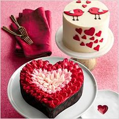 a heart - shaped cake sits on plates next to other desserts and napkins