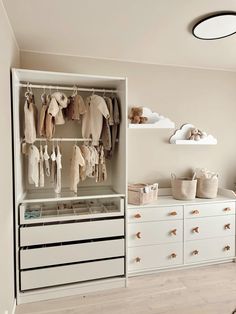 an organized closet with white drawers and baby clothes hanging on the rails, in front of a window