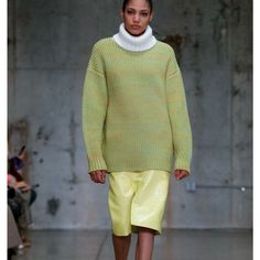 a model walks down the runway wearing yellow shorts and a green sweater with white collar