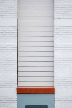 an orange and blue fire hydrant sitting in front of a white brick wall