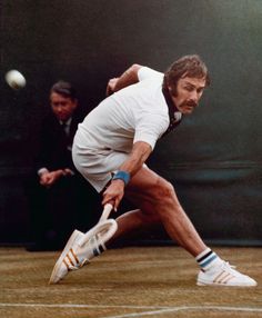 a man swinging a tennis racquet at a ball on a court with two men in the background