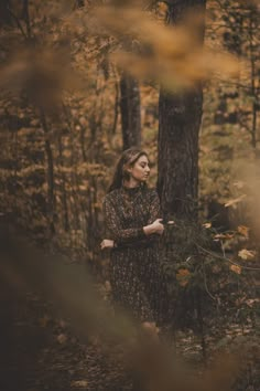 a woman is standing in the woods with her arms crossed and looking off into the distance