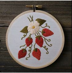 a white embroidered wall hanging with strawberries and daisies on it, in front of a wooden background