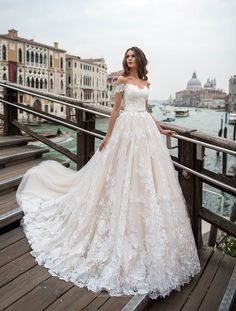 a beautiful woman in a wedding dress standing on a bridge near the water and buildings